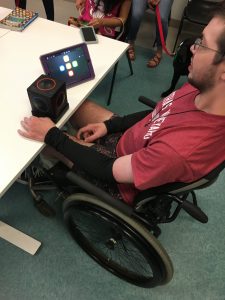 A young man sitting in a wheelchair plays with Skoog and iPad.