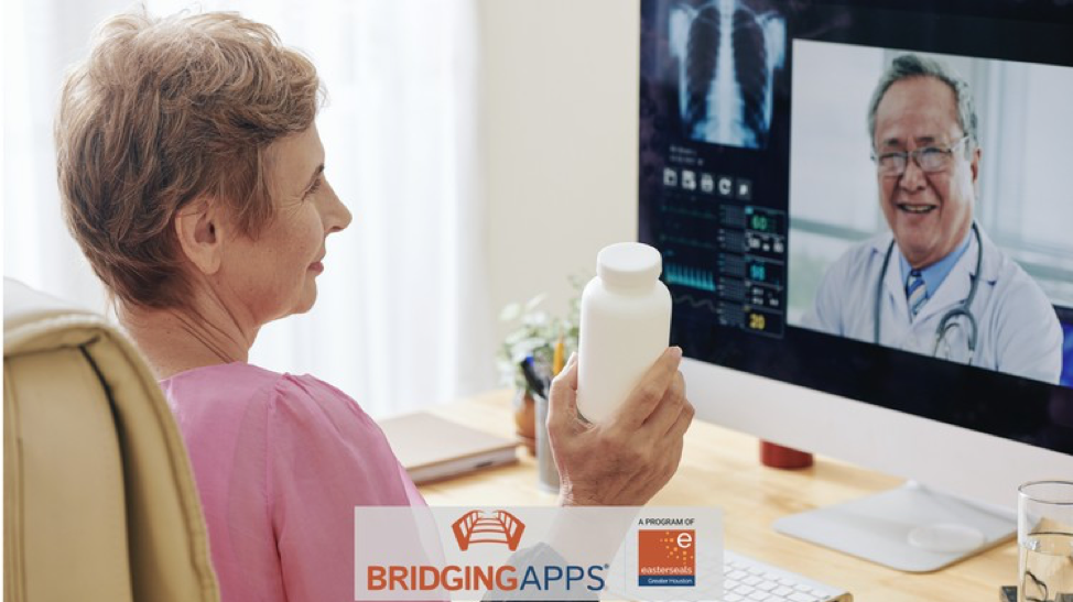 Older adult female sitting in front of computer holding pill bottle. Provider on computer screen.