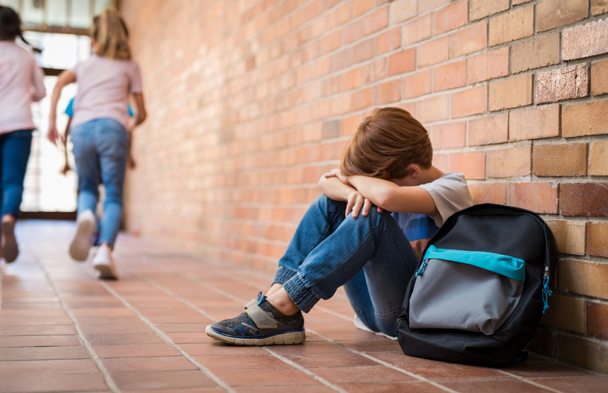 boy sitting against a wall with head down on knees