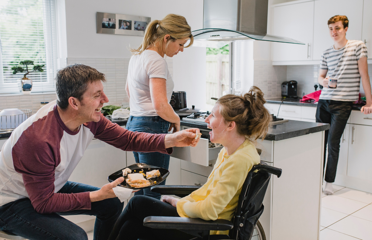 young adult female in wheelchair with middle age male feeding her