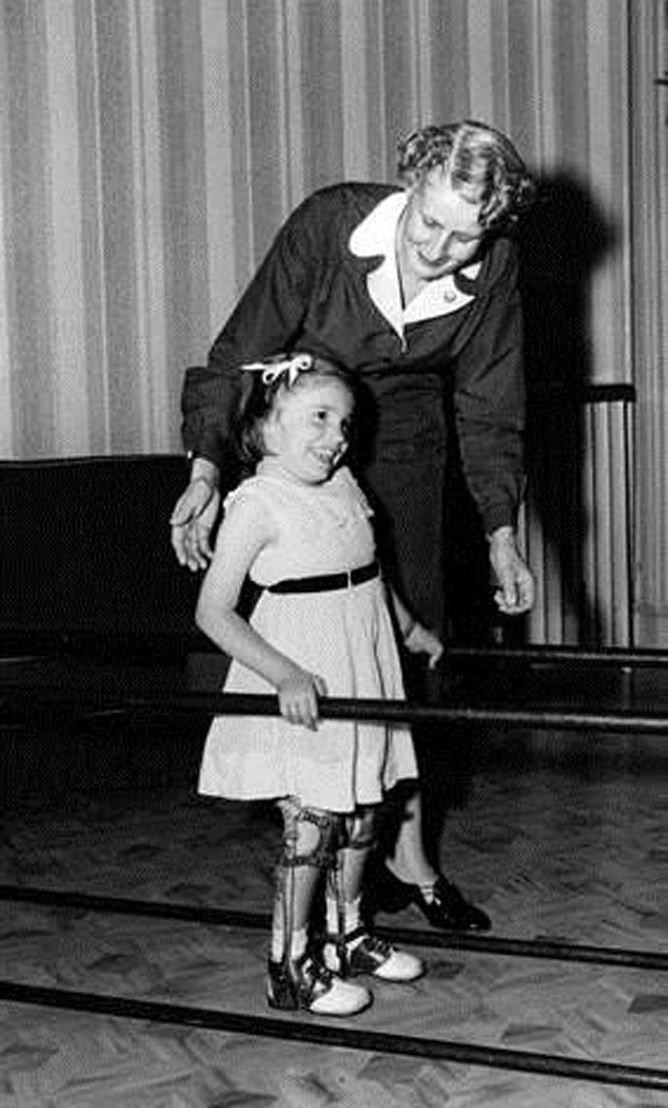 black and white photo of young girl with leg braces with physical therapist