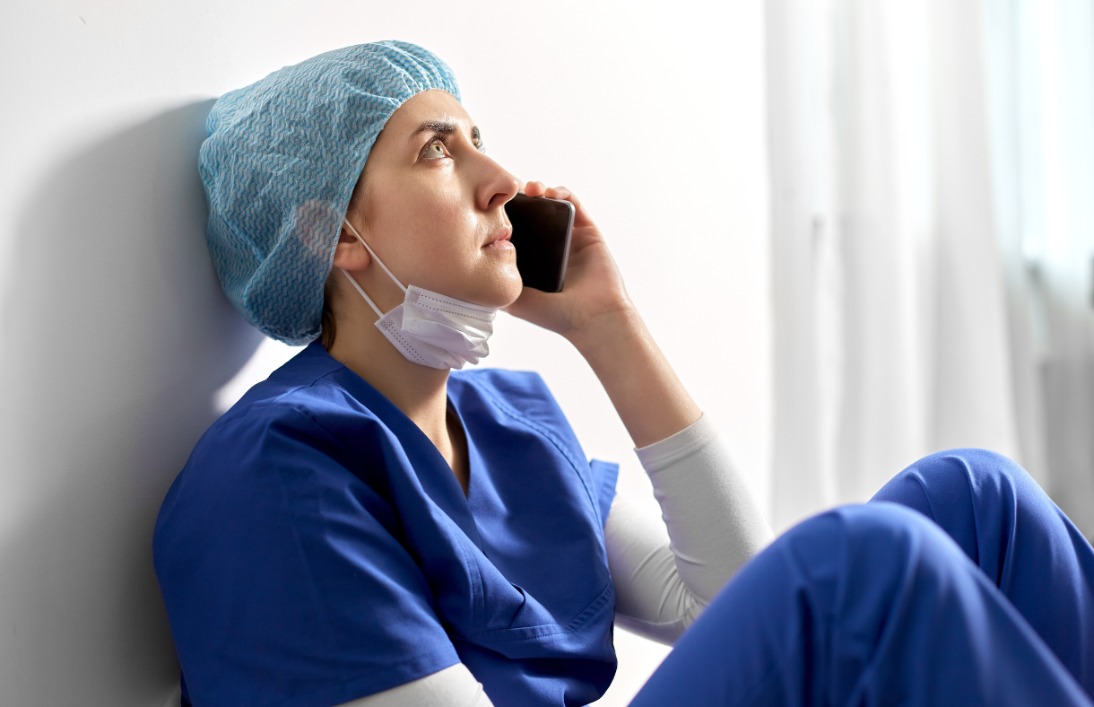 female doctor talking on phone sitting against wall on floor