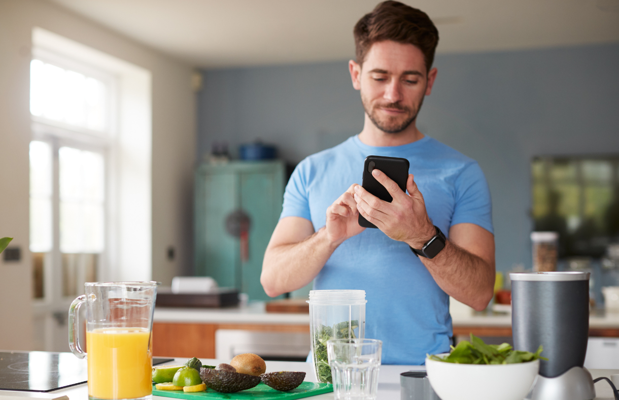 man using phone while making smoothie in kitchen