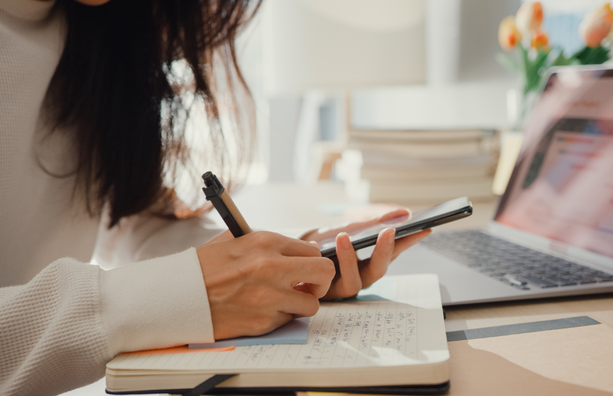 woman holding phone while writing in a planner