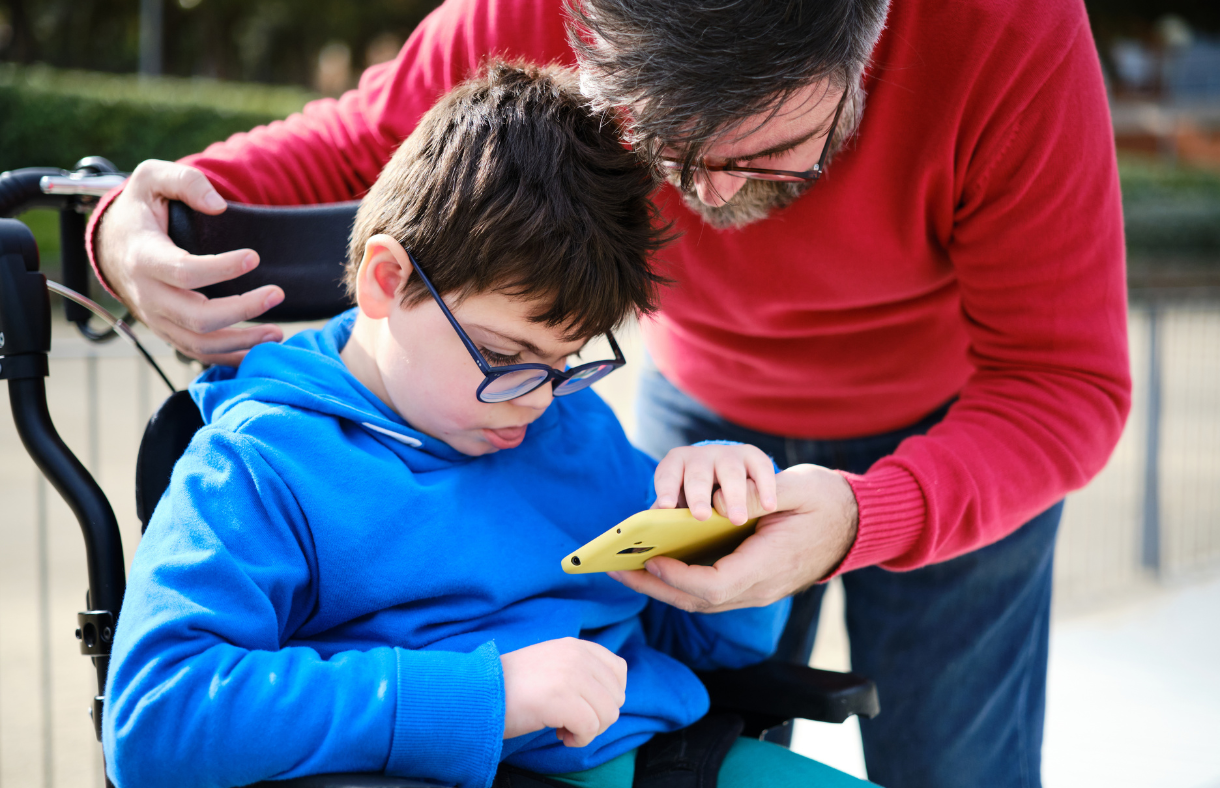 boy in wheelchair with dad helping him look at phone