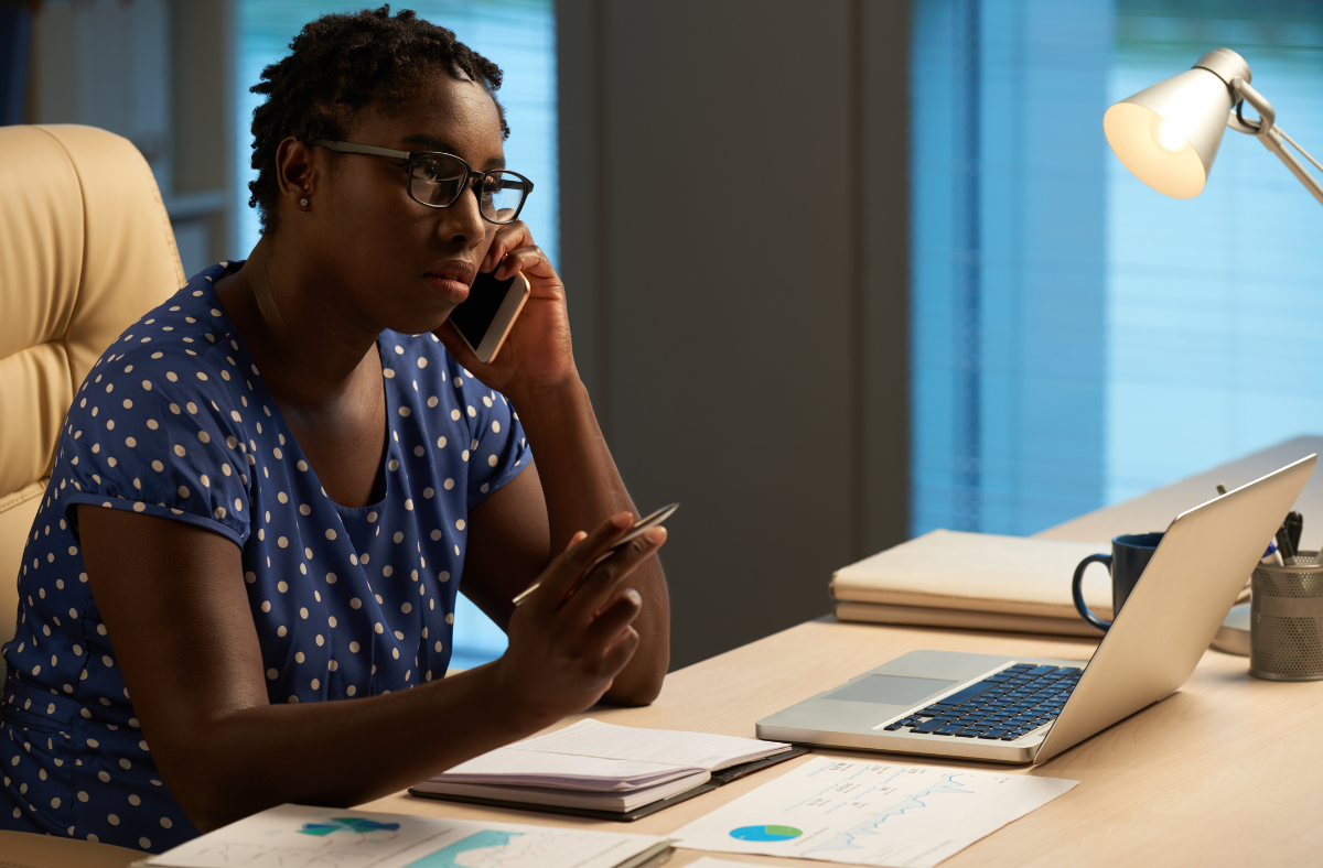 woman sitting in office with phone to her ear looking at laptop