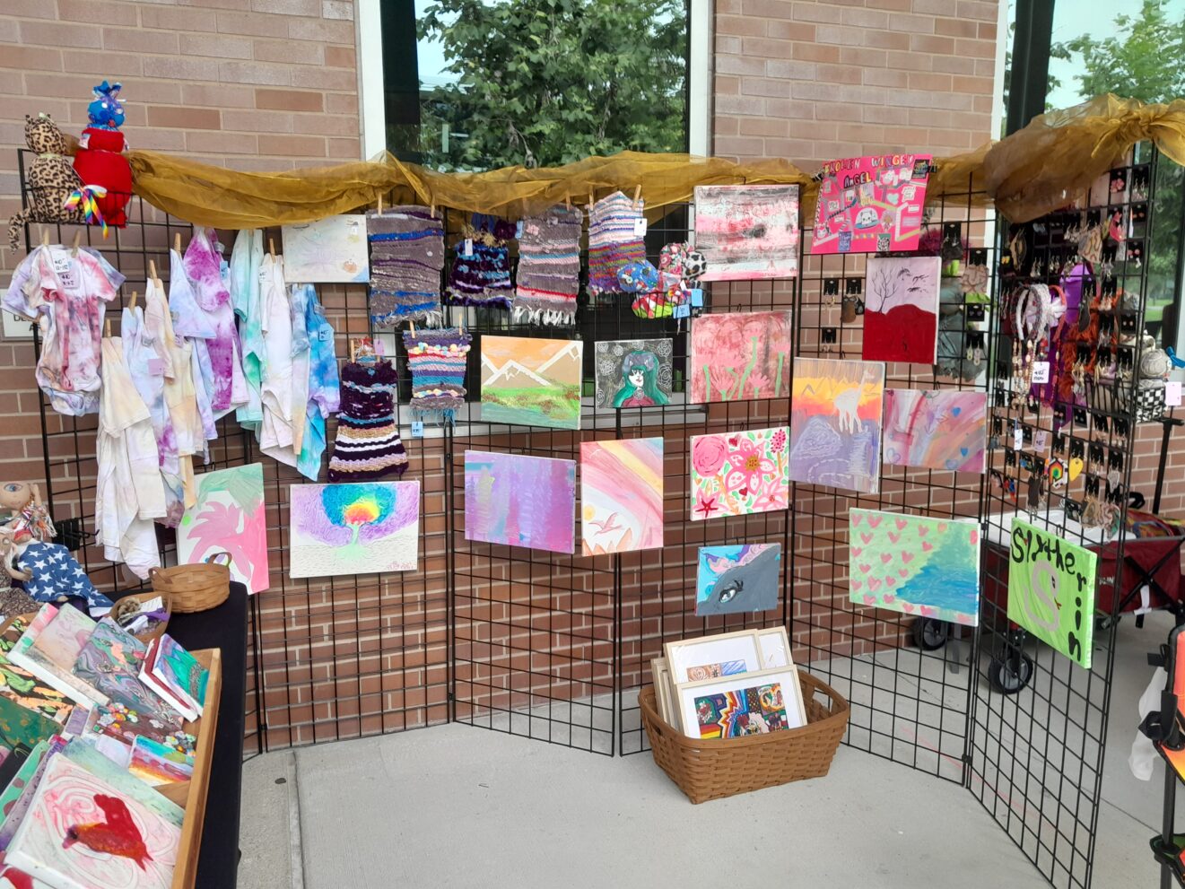 Outdoor crafts display of Tatum's paintings, textiles, and tie-dyed shirts.