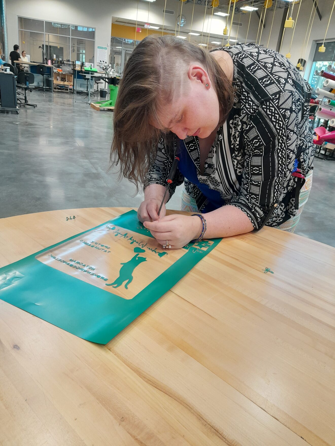 Tatum working on teal-green stencil of cat reaching up for heart image. 