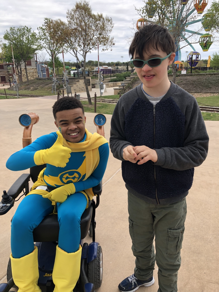 Visitor posing with park volunteer, who is in wheelchair and in blue-and-yellow hero costume