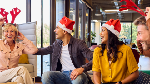 4 adults wearing santa hats sitting in a office