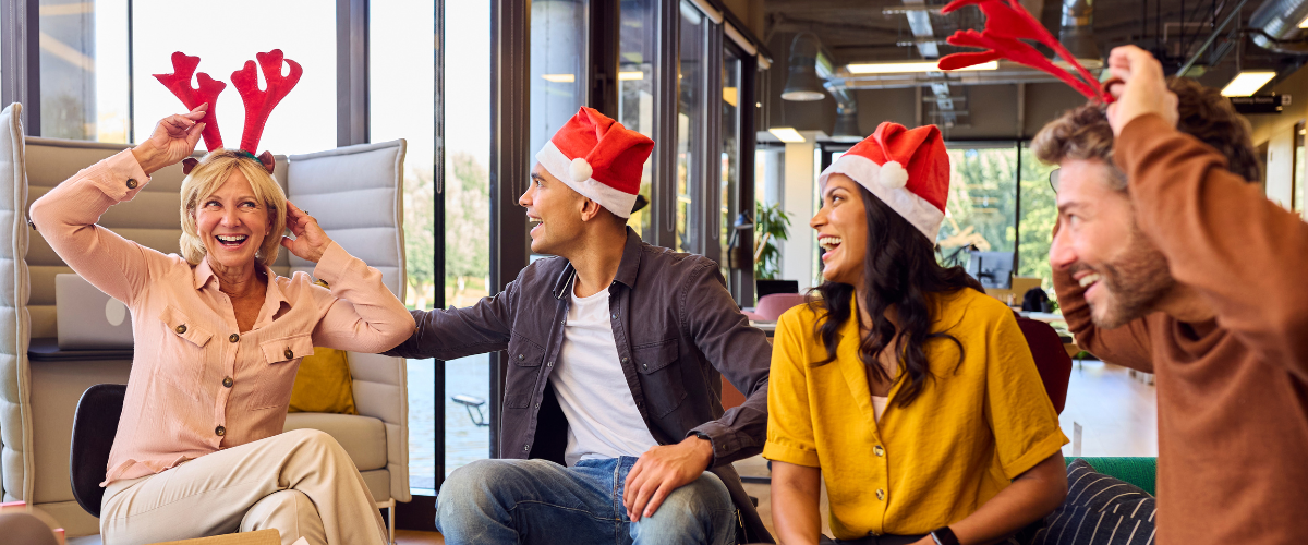 4 adults wearing santa hats sitting in a office