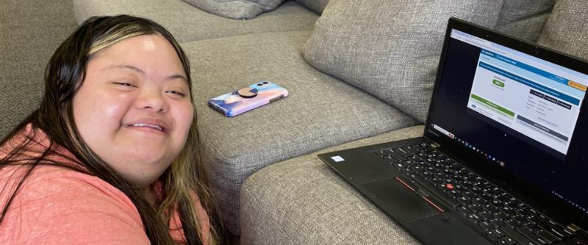 young adult girl with down syndrome smiling next to laptop