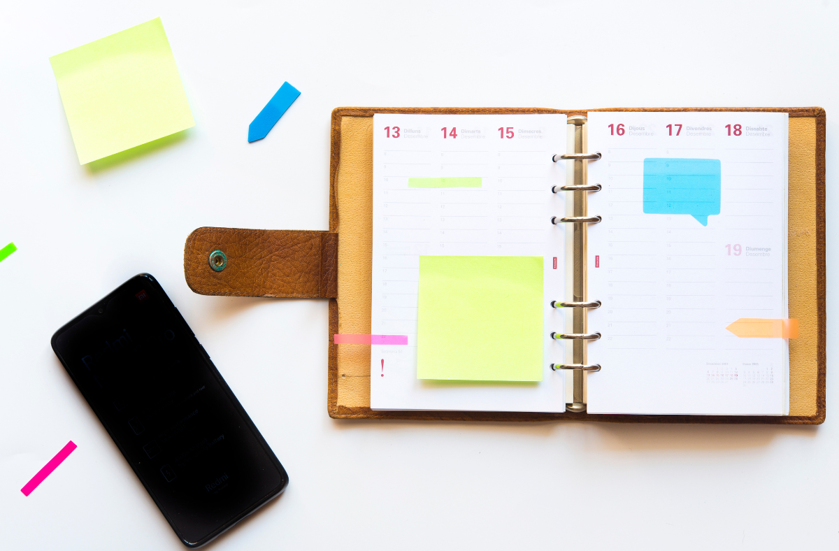 paper planner with sticky notes sitting on desk next to smart phone