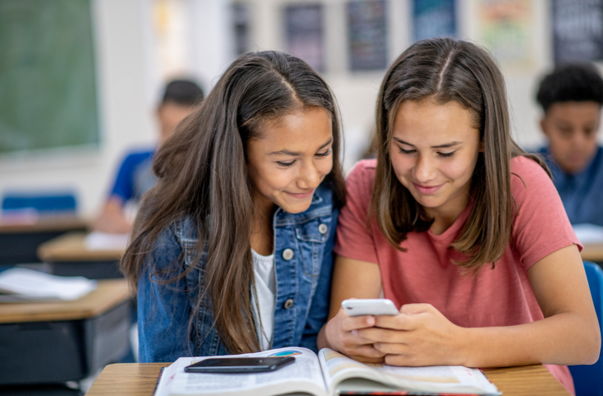 two middle school aged girls looking at phone together in class