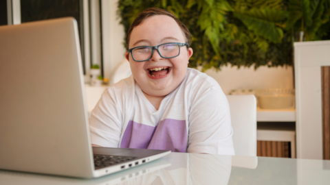 smiling child with down syndrome sitting at desk with laptop
