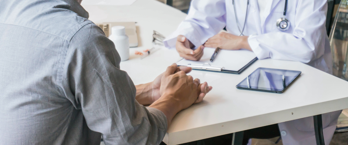 2 sets of male hands, one wearing medical coat, sitting at table with clipboard and ipad