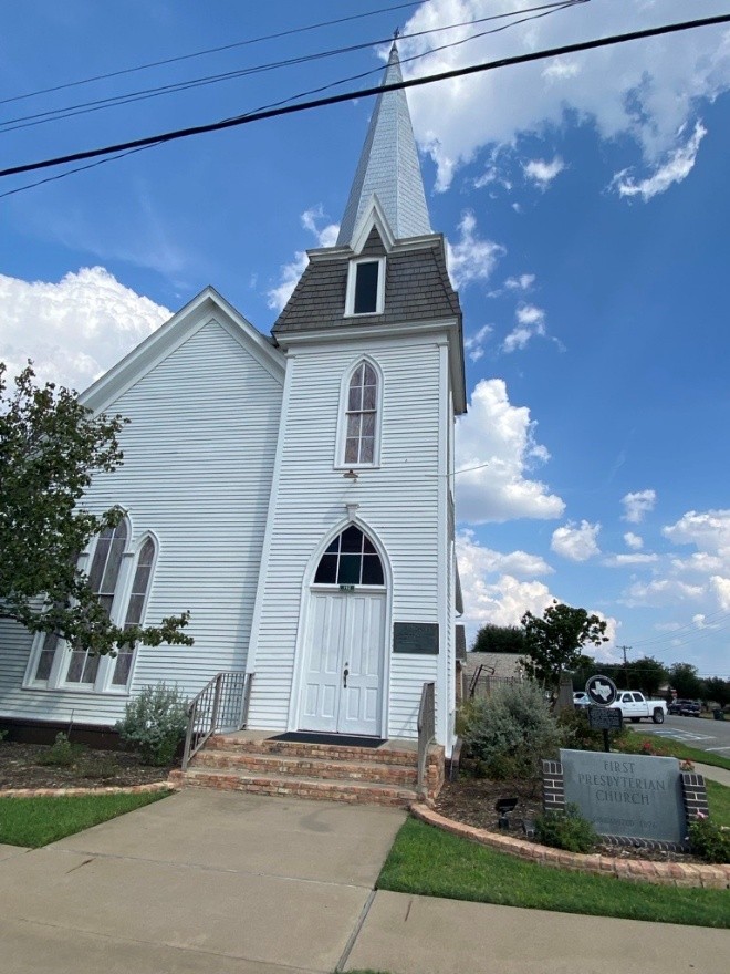 White country church with high steeple. A street-level, brick-framed sign to the right reads, "First Presbyterian Church."