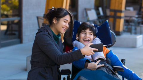 boy in wheelchair being shown a smartphone by young adult