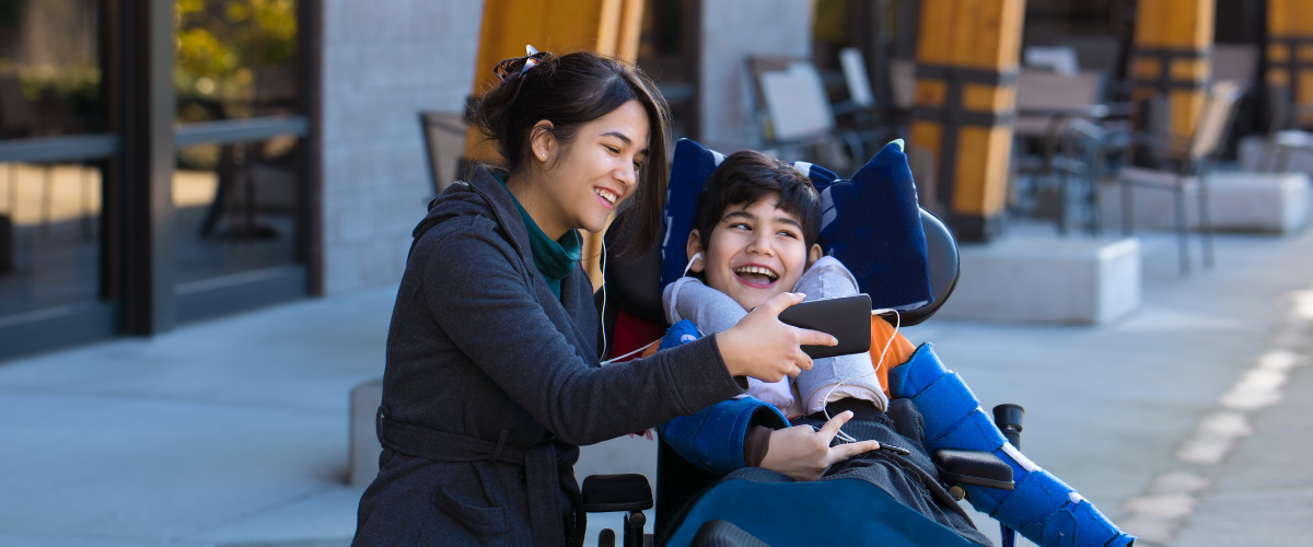 boy in wheelchair being shown a smartphone by young adult