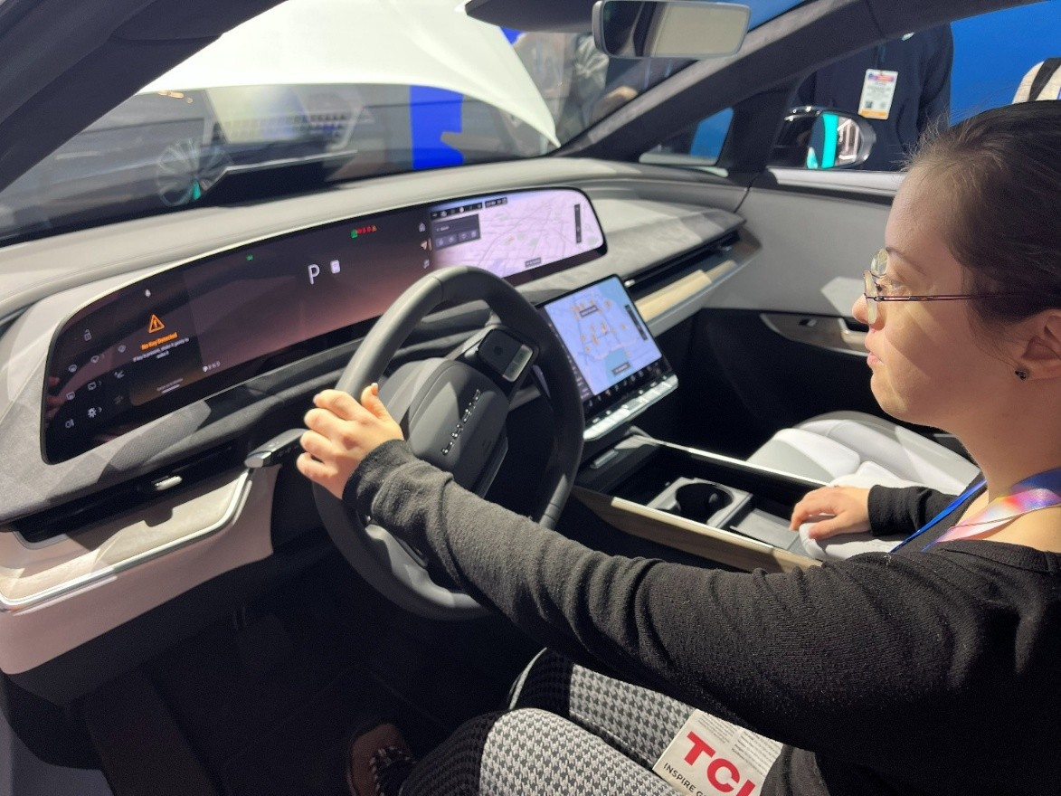 Left-profile close-up of Sarah (young woman with brown hair and glasses) sitting behind the wheel of a car.