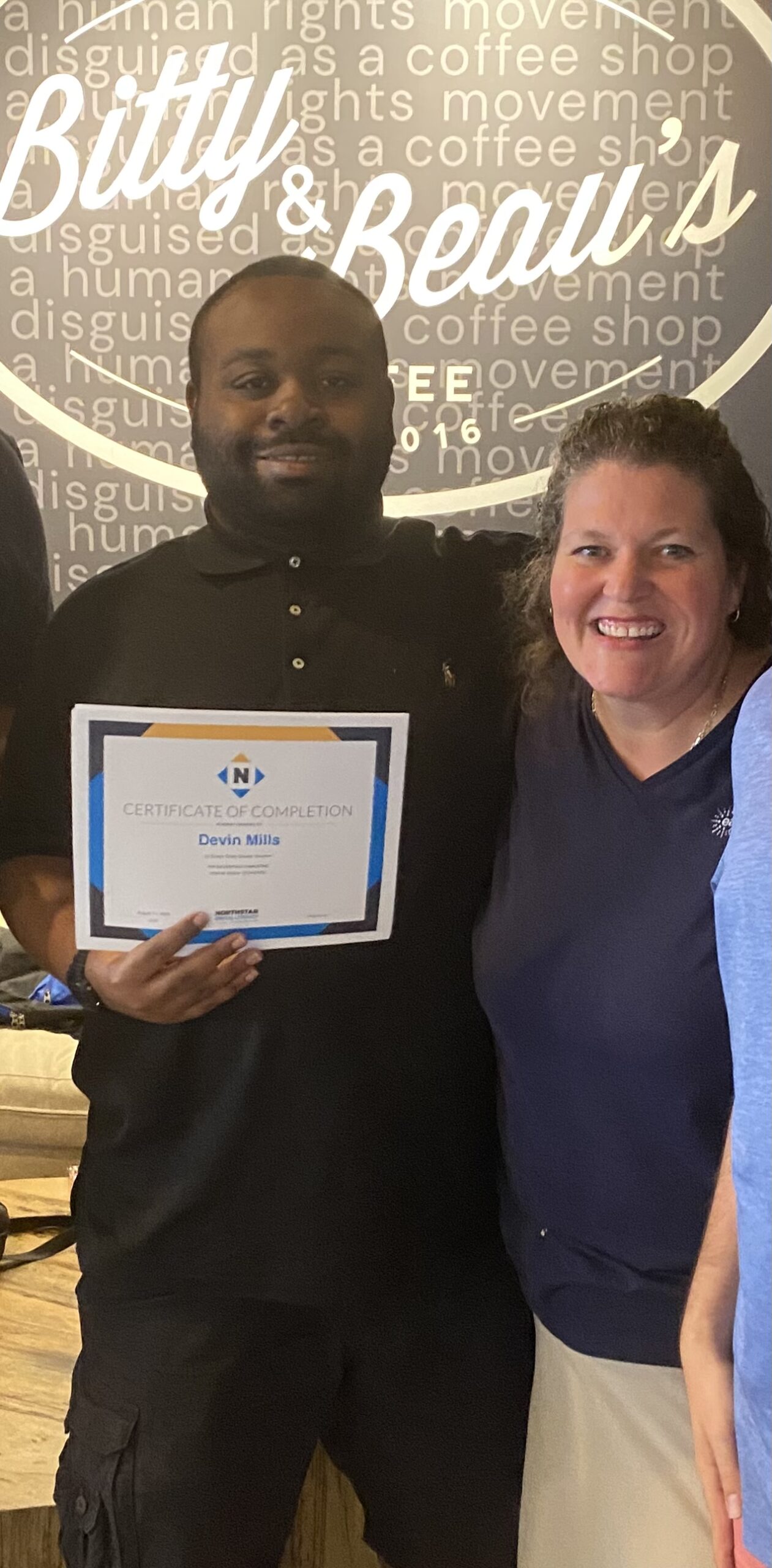 Young man and woman smiling for camera holding a certificate at coffee shop