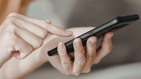 close up of one hand holding phone while other taps screen