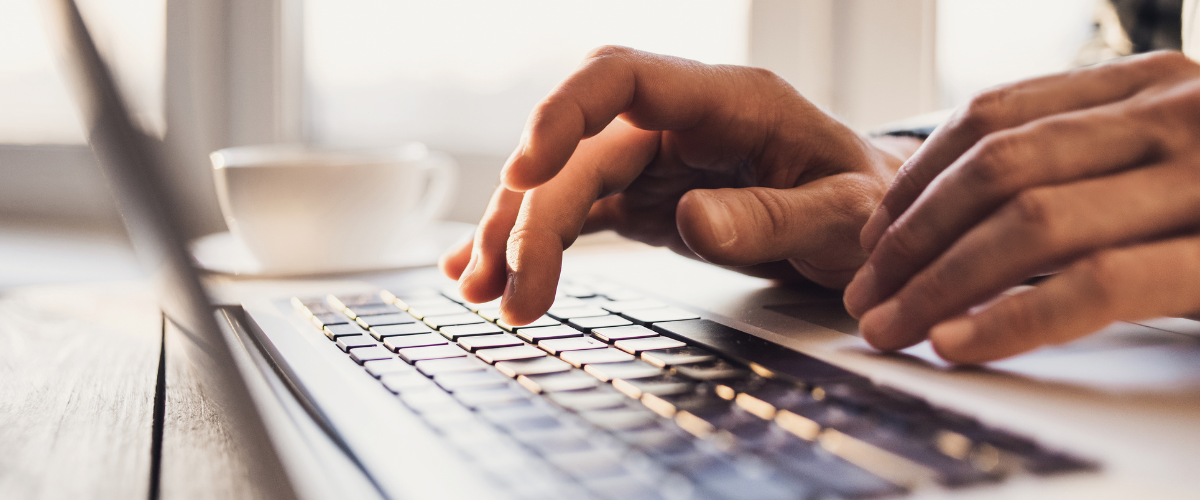 Hands typing on a laptop keyboard with a blurred cup in the background.