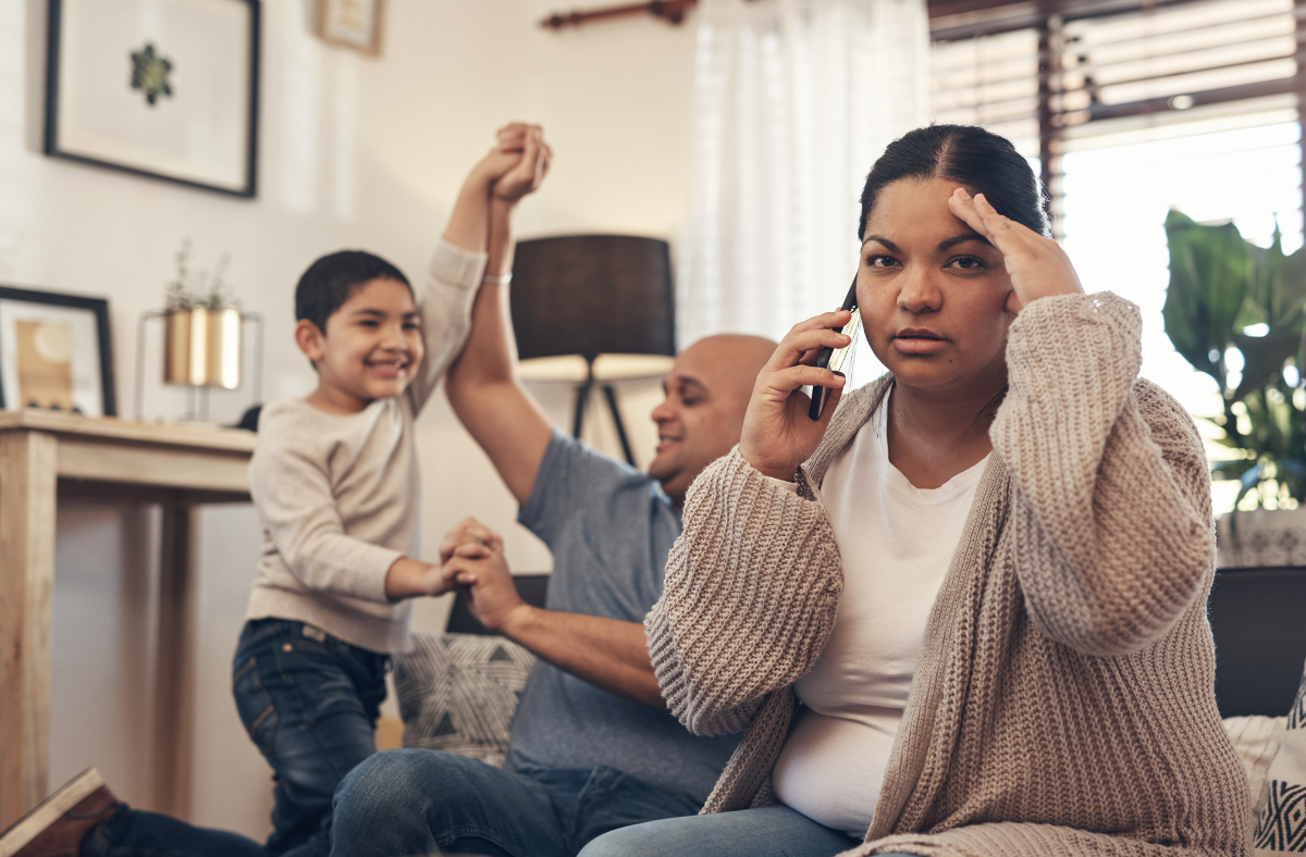 stressed looking parent on phone with dad and daughter playing in background