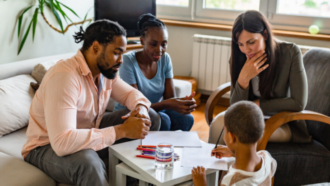 child sitting at table writing with parents and therapist looking on