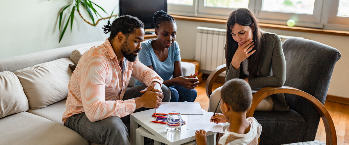 child sitting at table writing with parents and therapist looking on