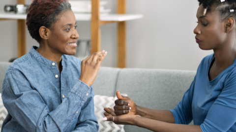2 women sitting on couch using sign language to communicate