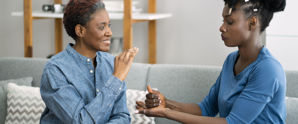 2 women sitting on couch using sign language to communicate