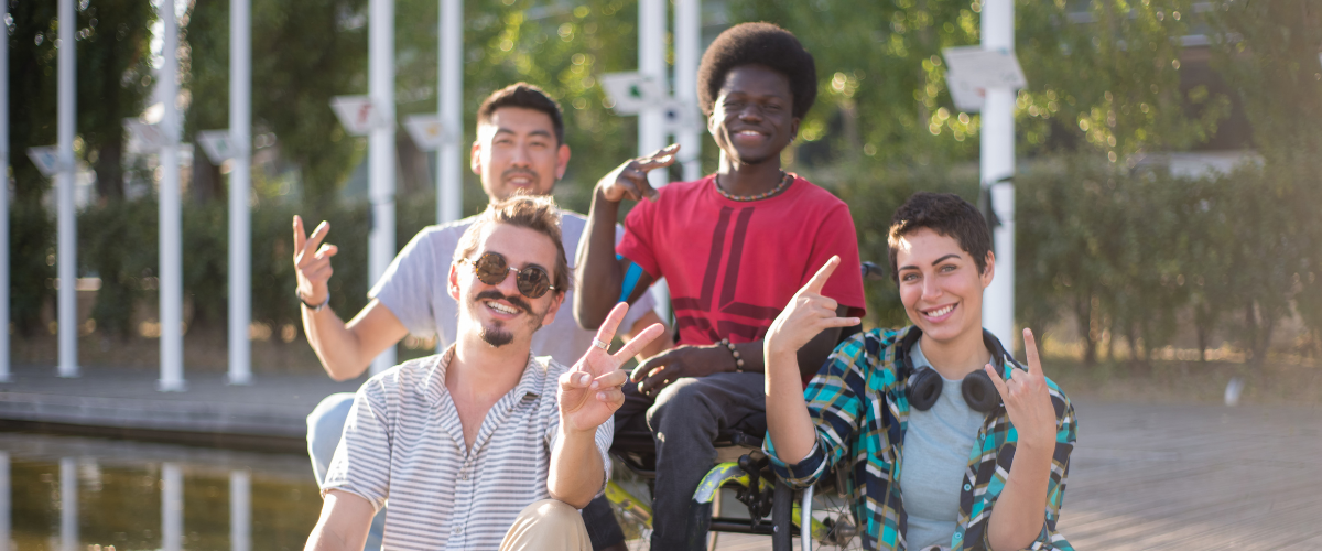 4 friends outside smiling and posing for camera, middle friend in sitting in wheelchair