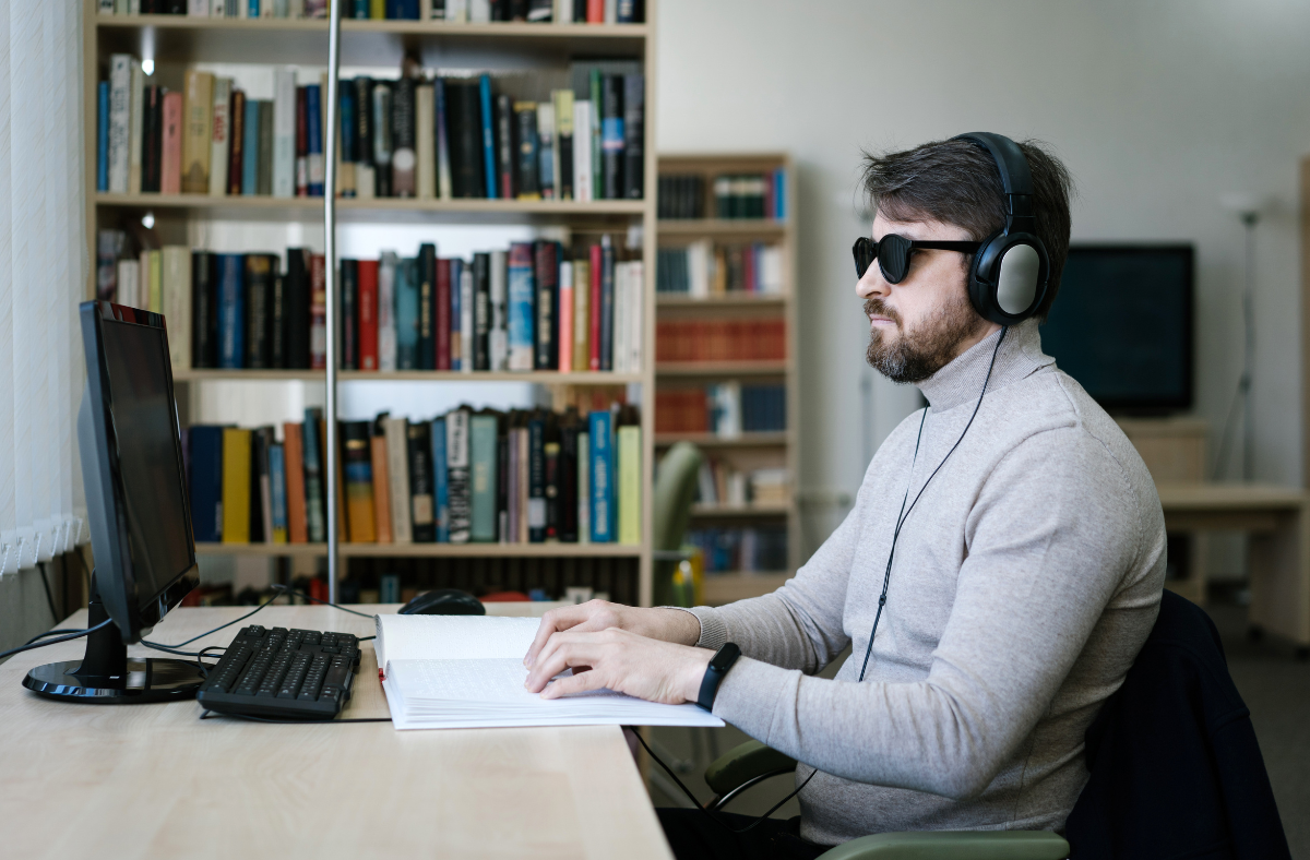 man sitting in front of bookshelf at computer wearing headphones and glasses