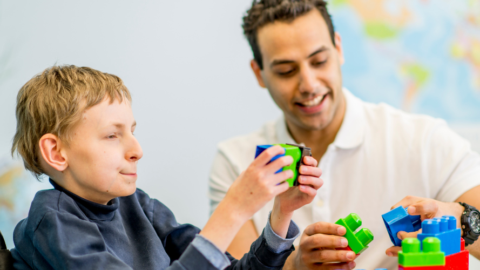 young-man-in-wheelchair-putting-large-plastic-blocks-together-with-male-therapist