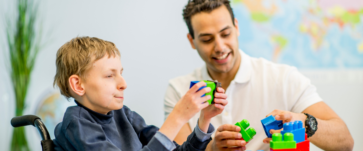 young-man-in-wheelchair-putting-large-plastic-blocks-together-with-male-therapist