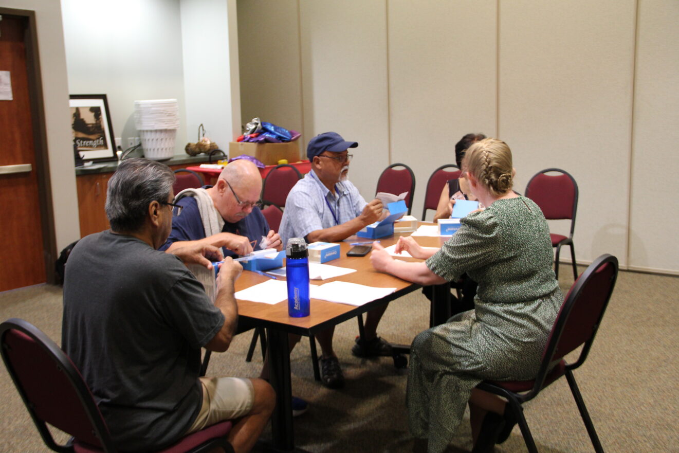 Five people, three only partly visible, seated around rectangular table. Ceretone boxes are laid out in front of them.
