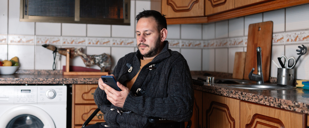 man in wheelchair in kitchen looking at phone in hand